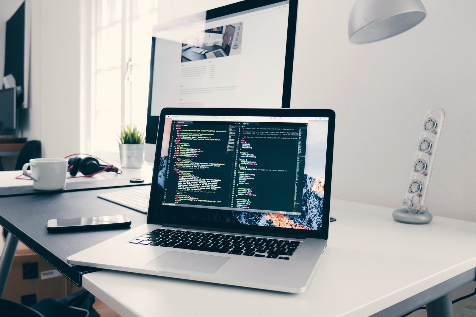 A laptop showing code on a white desk in a bright office